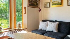 A modern living room with a sofa, a wooden coffee table, and a floor lamp. There is a window with a view of greenery outside. - 4 Star Holiday Home in Annerstad (Annerstad)