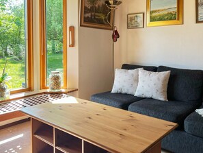 A modern living room with a sofa, a wooden coffee table, and a floor lamp. There is a window with a view of greenery outside. - 4 Star Holiday Home in Annerstad (Annerstad)