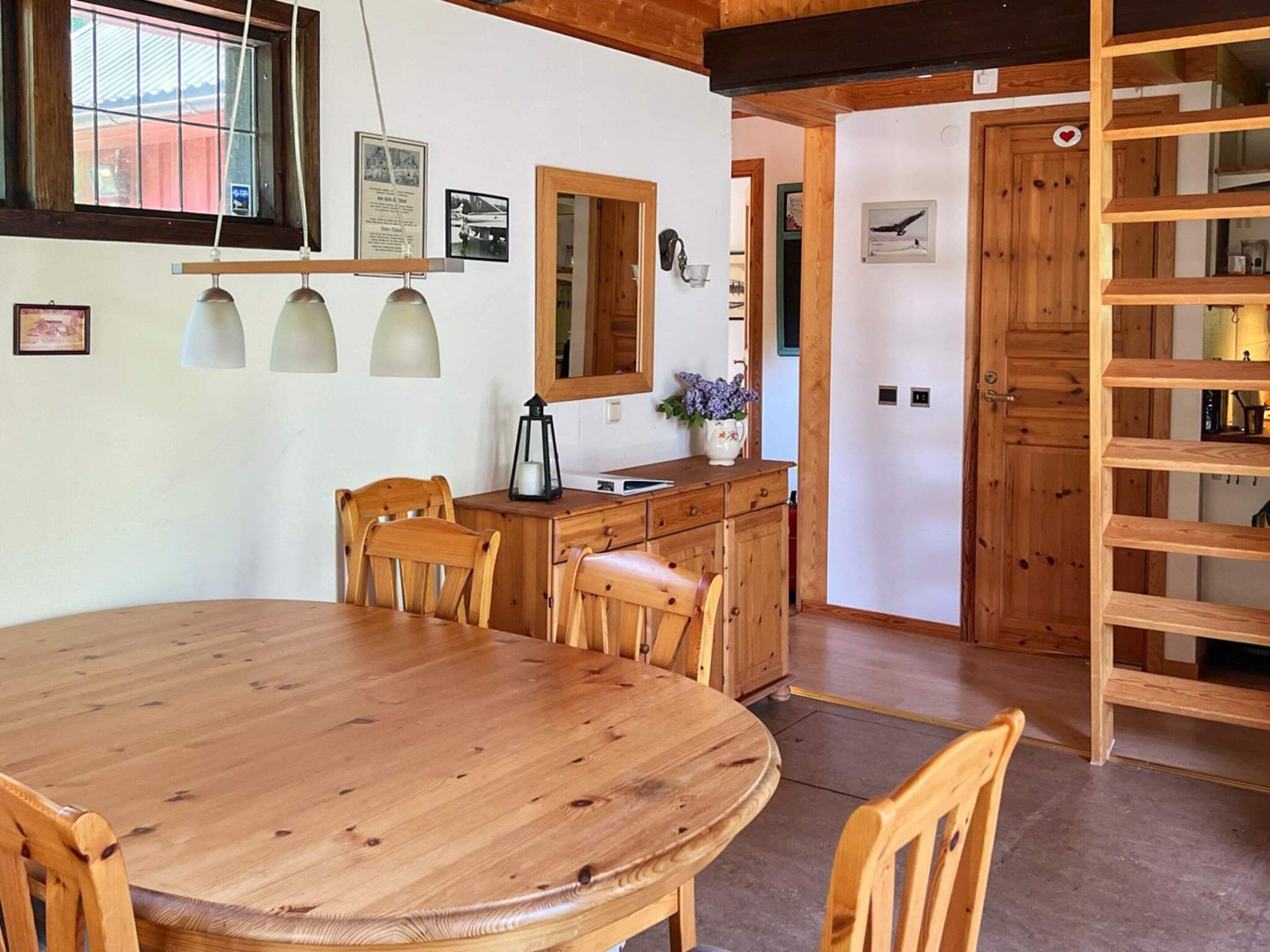 Una mesa de comedor de madera con sillas, una zona de cocina con un fregadero y armarios, y una estantería de madera.