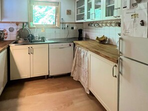 Une cuisine avec des meubles blancs, un plan de travail en bois, un lave-vaisselle et un réfrigérateur.
