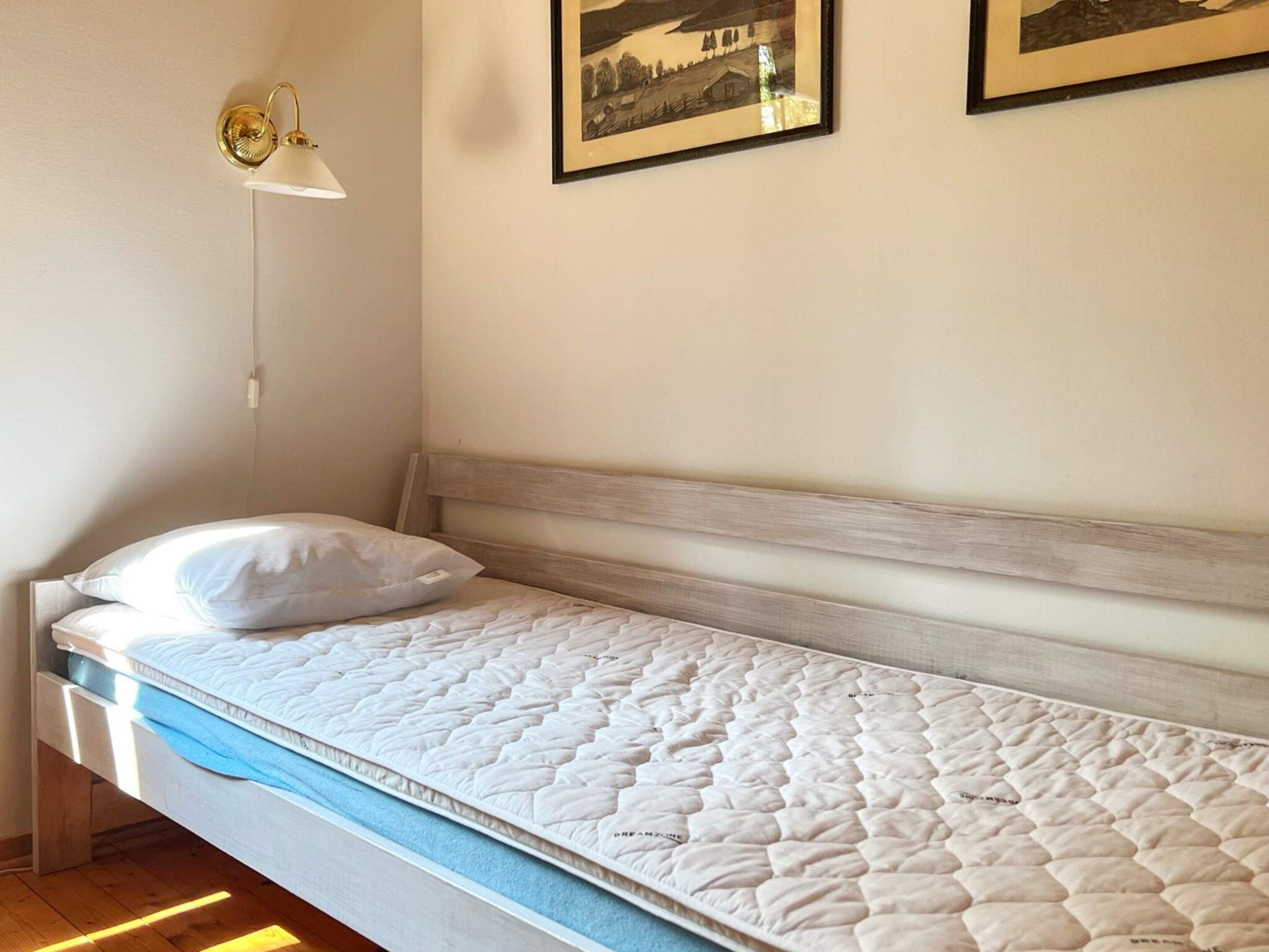 A single bed with a white mattress and a wooden headboard in a room with white walls.