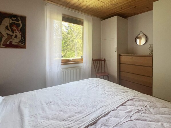 A bedroom with a bed, a wooden dresser, a chair, a window, and a painting on the wall. - 4 Star Holiday Home in Annerstad (Annerstad)