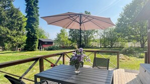 An outdoor deck with a table and chairs, a wooden railing, and a large umbrella. - 4 Star Holiday Home in Annerstad (Annerstad)