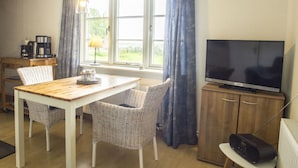 A cozy room with a wooden dining table, wicker chairs, a TV, and a radio on a cabinet. - Holiday Apartment Lugworm (Ockholm)