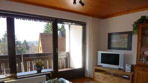 Ein Wohnzimmer mit Glastisch, Fernseher und Blick ins Freie.