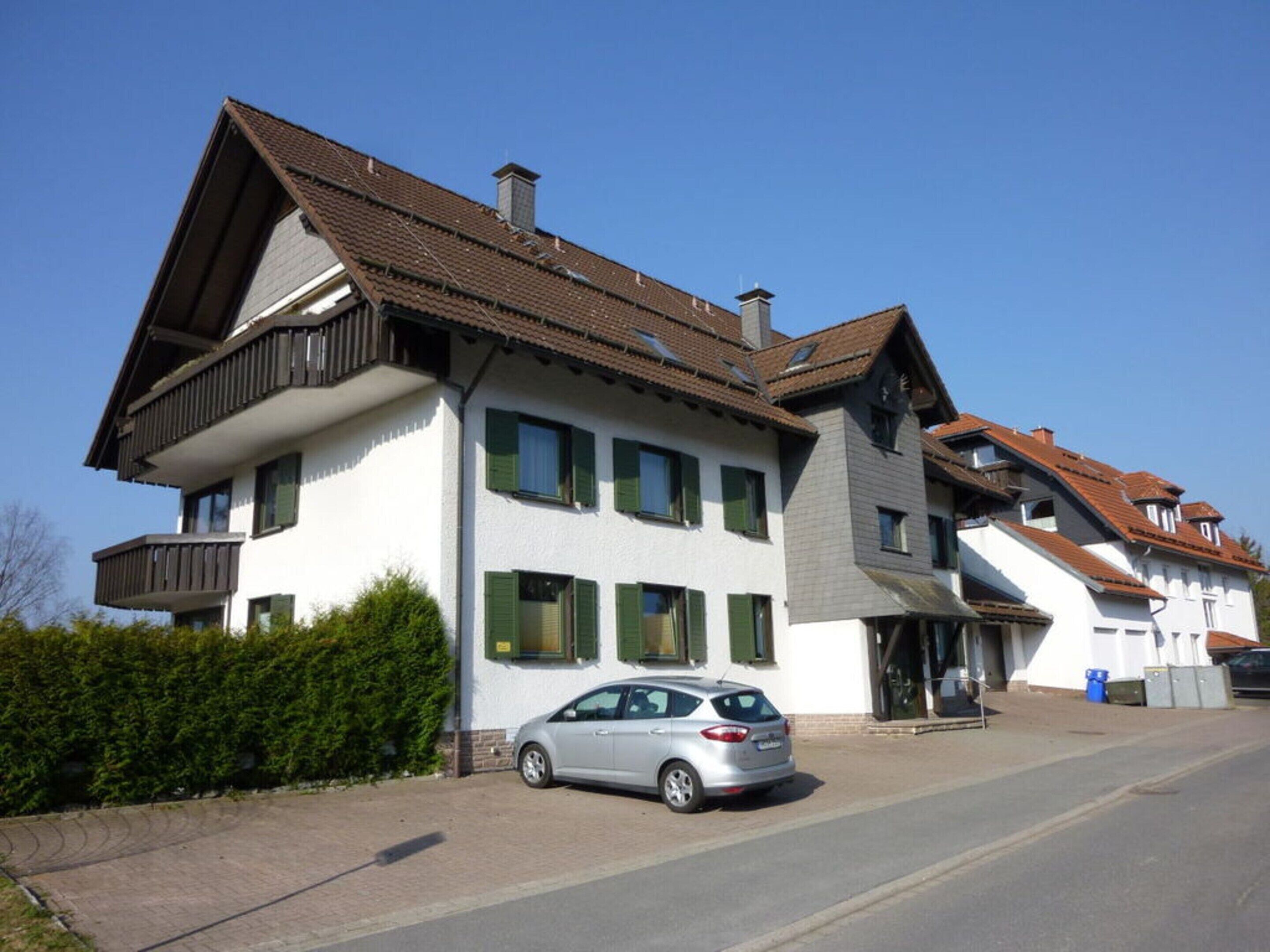 A two-story house with a balcony, a car parked in front, and a clear blue sky.