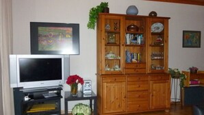 Ein Wohnzimmer mit Fernseher, Holzschrank und Teppich.