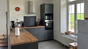 Et moderne køkken med lysegrå skabe, en træbordplade, et rustfrit stål emfang, en mikroovn, en ovn og et vindue med udsigt over et grønt landskab.