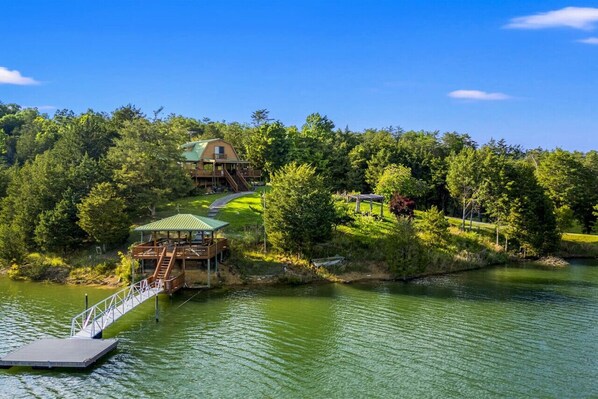 A lakeside lodge with a dock, a covered deck, and a building with a green roof.
