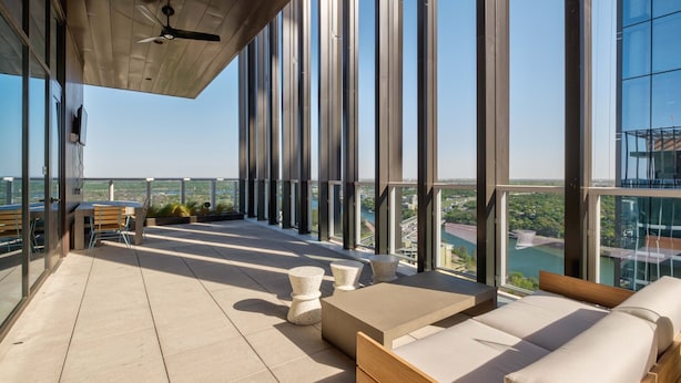 A modern rooftop terrace with a clear view of the cityscape, featuring a seating area with a table and chairs, and a ceiling fan.
