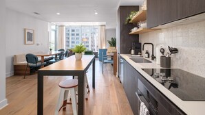 A modern kitchen with a dining area, wooden flooring, and a view of high-rise buildings.