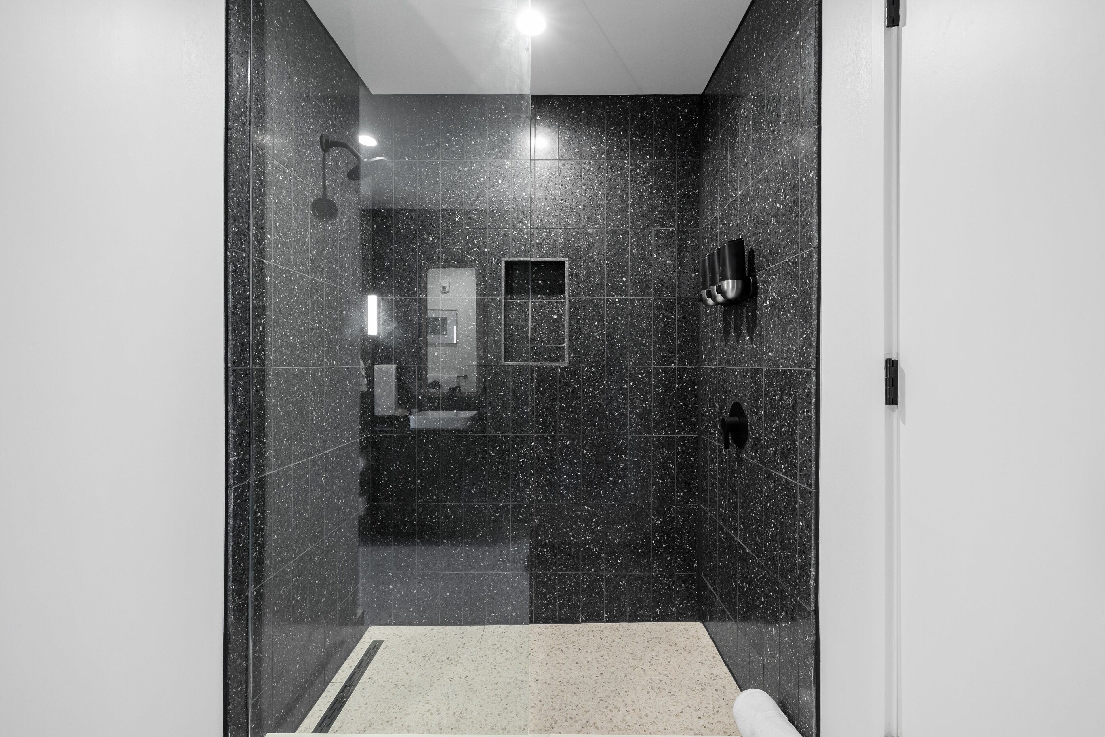 Un baño moderno con paredes de mármol oscuro, un lavamanos blanco y una cabina de ducha de vidrio.