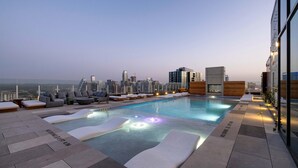 A rooftop pool with lounge chairs and a city skyline in the background.