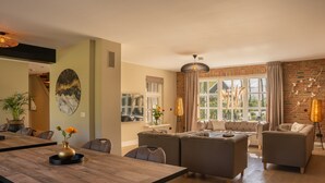 Un salon spacieux avec un grand canapé, une table à manger et des chaises, ainsi qu’un mur en briques.
