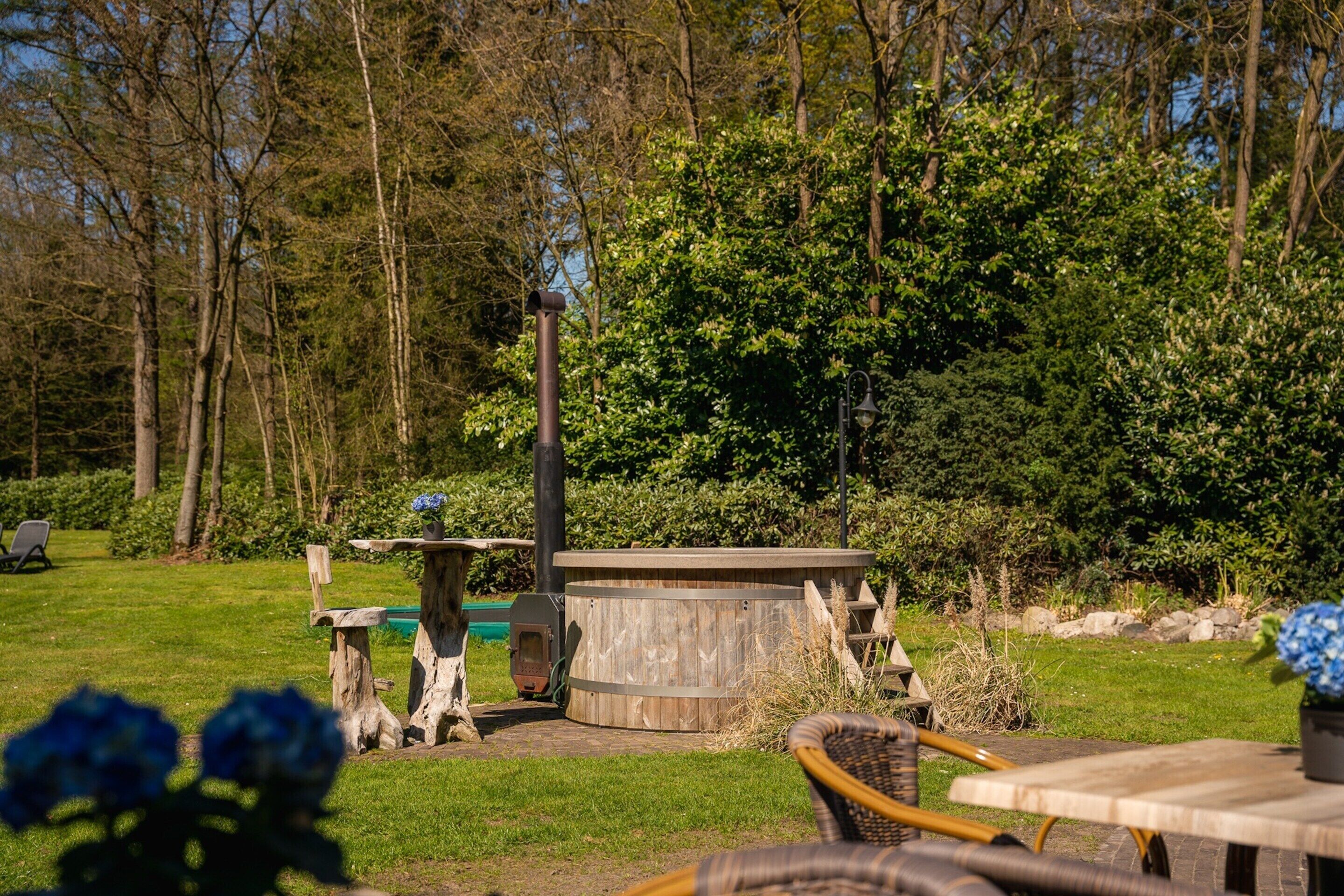 A rustic outdoor seating area with a wooden table and chairs, surrounded by lush greenery and trees.