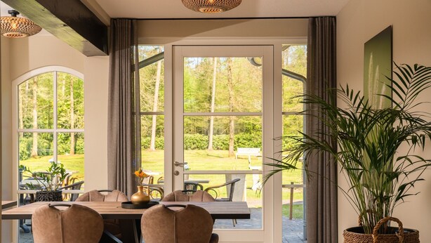Un coin repas avec une table et des chaises, une grande fenêtre donnant sur un jardin et une plante en pot.