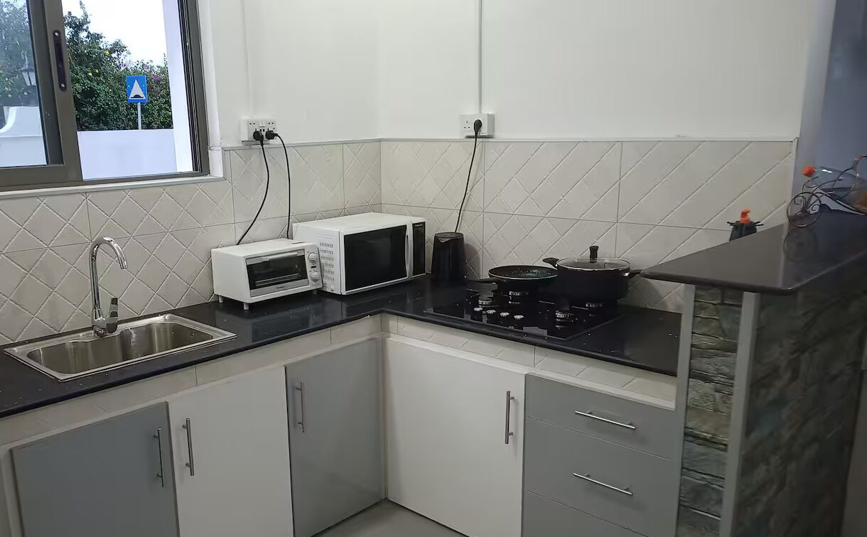 A kitchen with white cabinets, a black countertop, a sink, a microwave, a stove, and a window with a view of greenery.