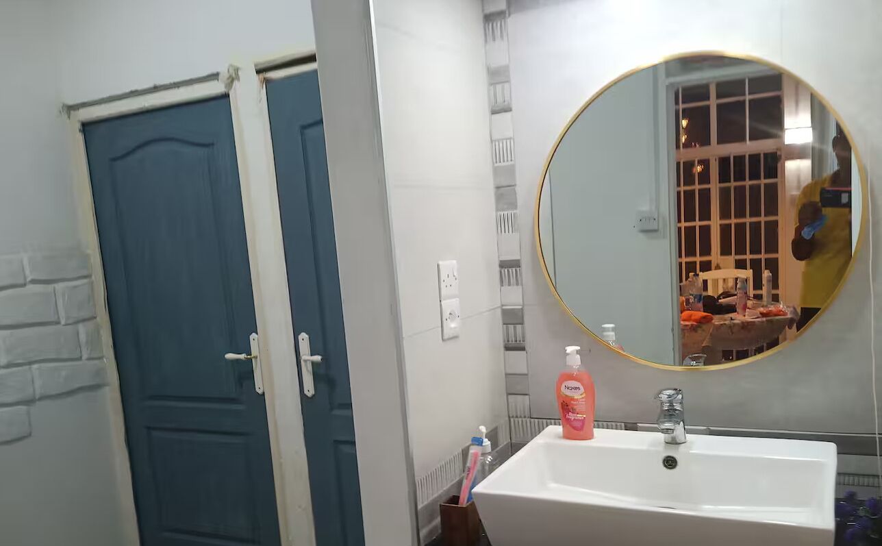 Un bagno con un lavandino bianco, uno specchio rotondo e una porta blu.