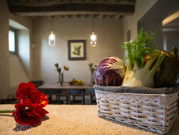 Une cuisine avec un panier en osier contenant des légumes, une fleur rouge et un tableau encadré accroché au mur.