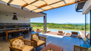 Un espace extérieur aménagé pour prendre les repas, avec vue sur une piscine et un jardin.