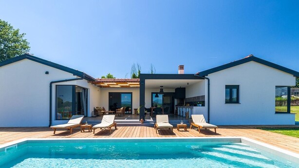 Une maison moderne dotée d’une piscine, de chaises longues et d’un patio couvert.