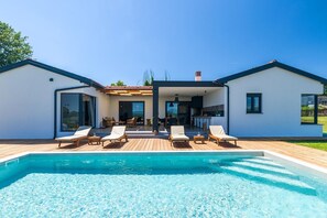 Ein modernes Haus mit Swimmingpool, Liegestühlen und einer überdachten Terrasse.