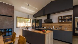 Une cuisine moderne dotée d’un îlot central, de meubles de rangement aux couleurs sombres, d’un plan de travail en bois et d’un coin repas avec des chaises en bois.