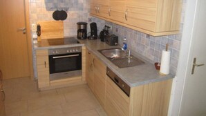 A compact kitchen with wooden cabinets, a built-in oven, a coffee maker, and a sink. - Holiday Home Seehase (Norden)