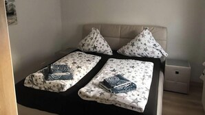 A bedroom with a bed, two pillows, a nightstand, and a small bedside table. - Holiday Home Seehase (Norden)