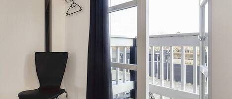 Een kamer met een zwarte stoel, een raam met uitzicht op een terras en een kapstok aan de muur.