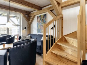 Ein modernes Wohnzimmer mit einer Holztreppe, einem schwarzen Ledersofa und einem Gemälde an der Wand.