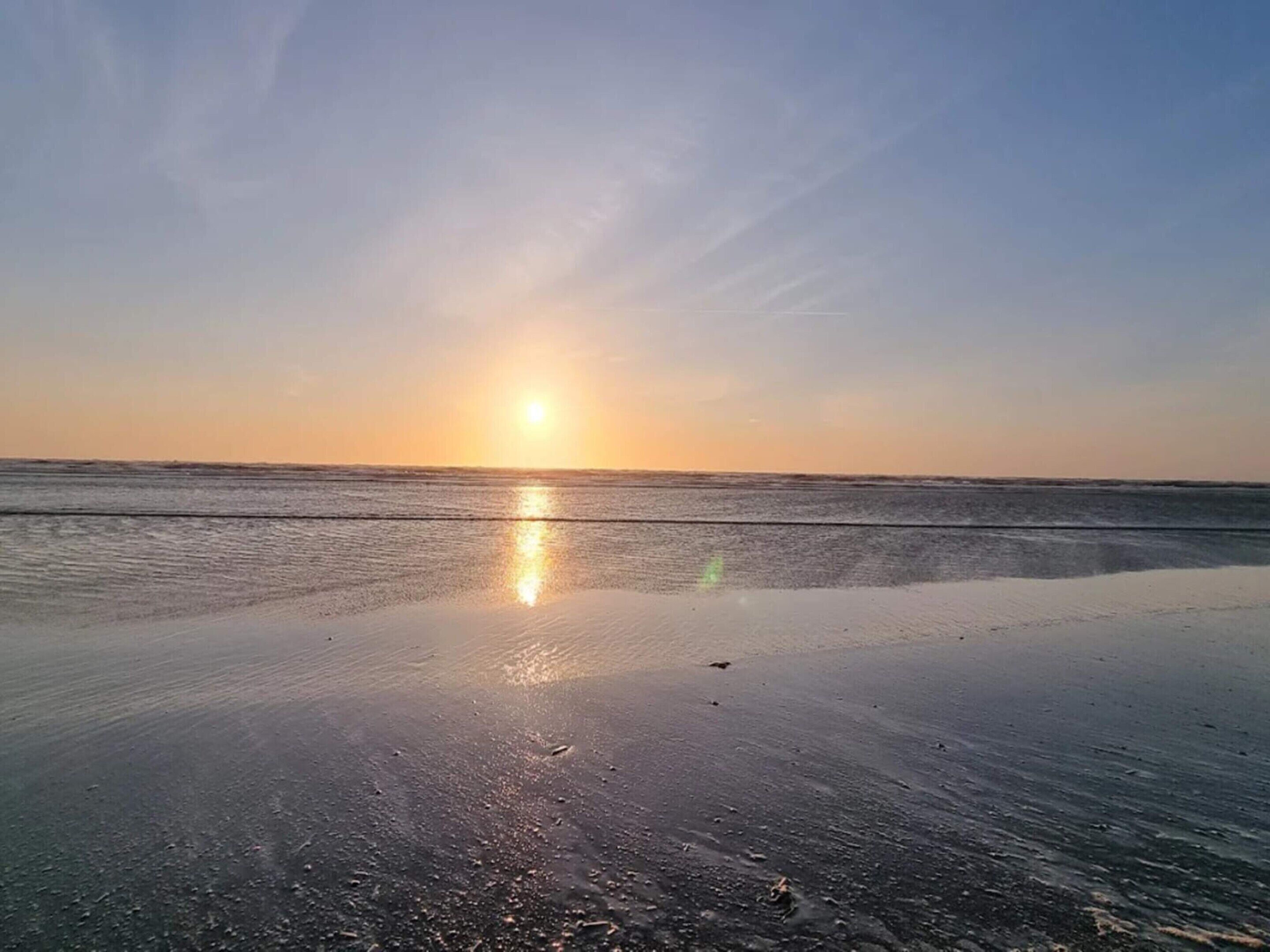 En strand vid solnedgången med stilla vatten som speglar solen.
