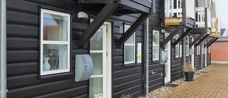 A row of black wooden houses with white window frames, a mailbox, and a small garden area with potted plants.