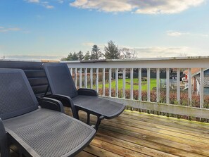 A wooden deck with two chairs and a table, overlooking a green lawn and a white fence. - 4 Person Holiday Home in Blavand (Blavand)