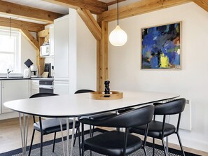 A modern kitchen with white cabinets, a dining table with four chairs, and a hanging light fixture. - 4 Person Holiday Home in Blavand (Blavand)