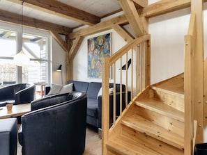 A modern living room with a staircase, leather chairs, a sofa, and a painting on the wall.
