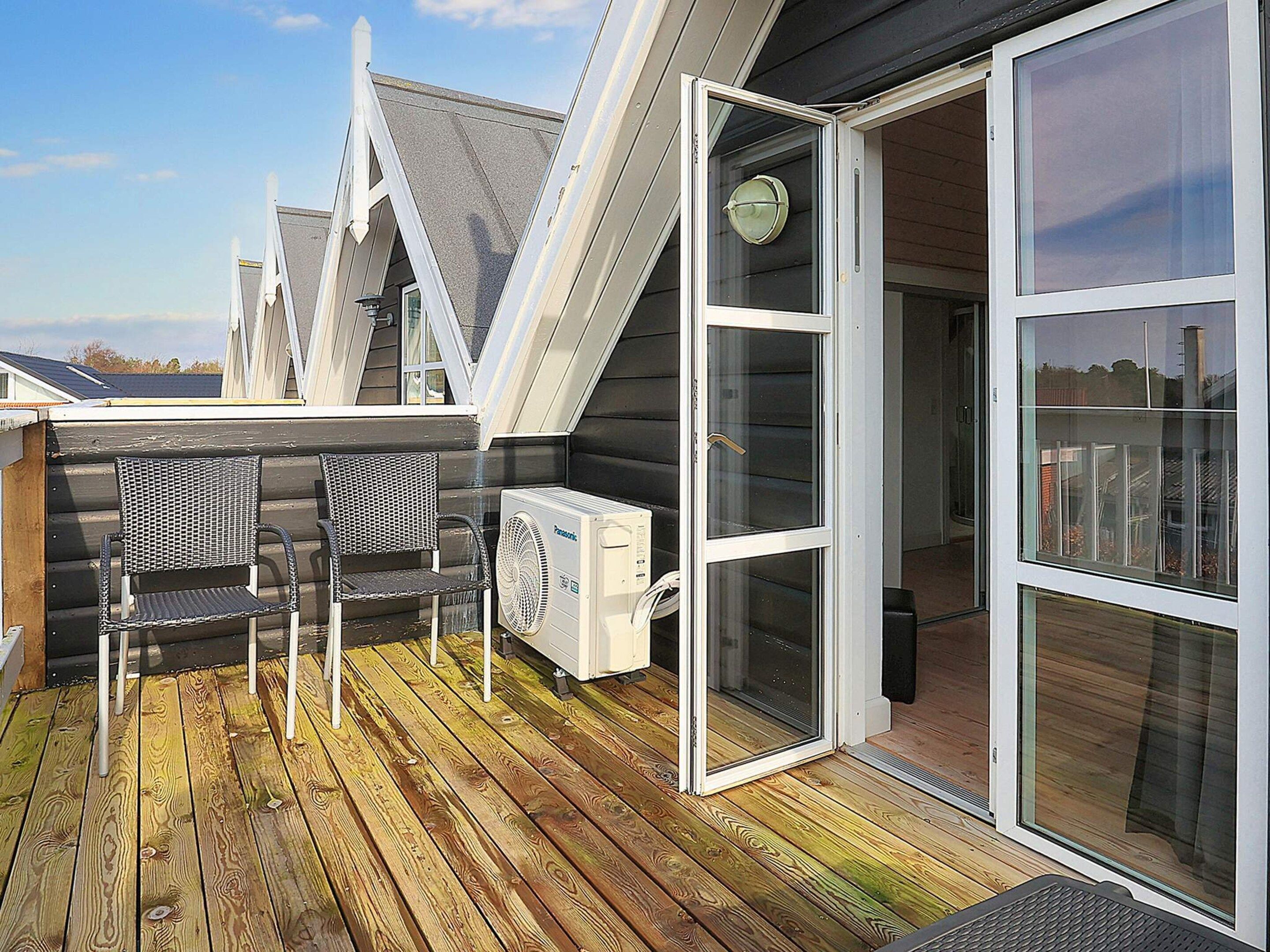 A deck with two chairs and a table, a sliding glass door, and an air conditioning unit.