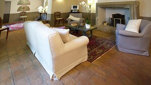 A living room with a white sofa, a grey armchair, a coffee table, and a fireplace. - Belvilla by OYO Villa Topazio REQ (Cortona)