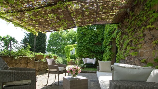 An outdoor patio area with wicker furniture, a white sofa, and a table with a vase of flowers. - Belvilla by OYO Villa Topazio REQ (Cortona)