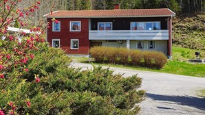 Ett tvåvåningshus med röd fasad och vita detaljer, omgivet av grönska och träd.