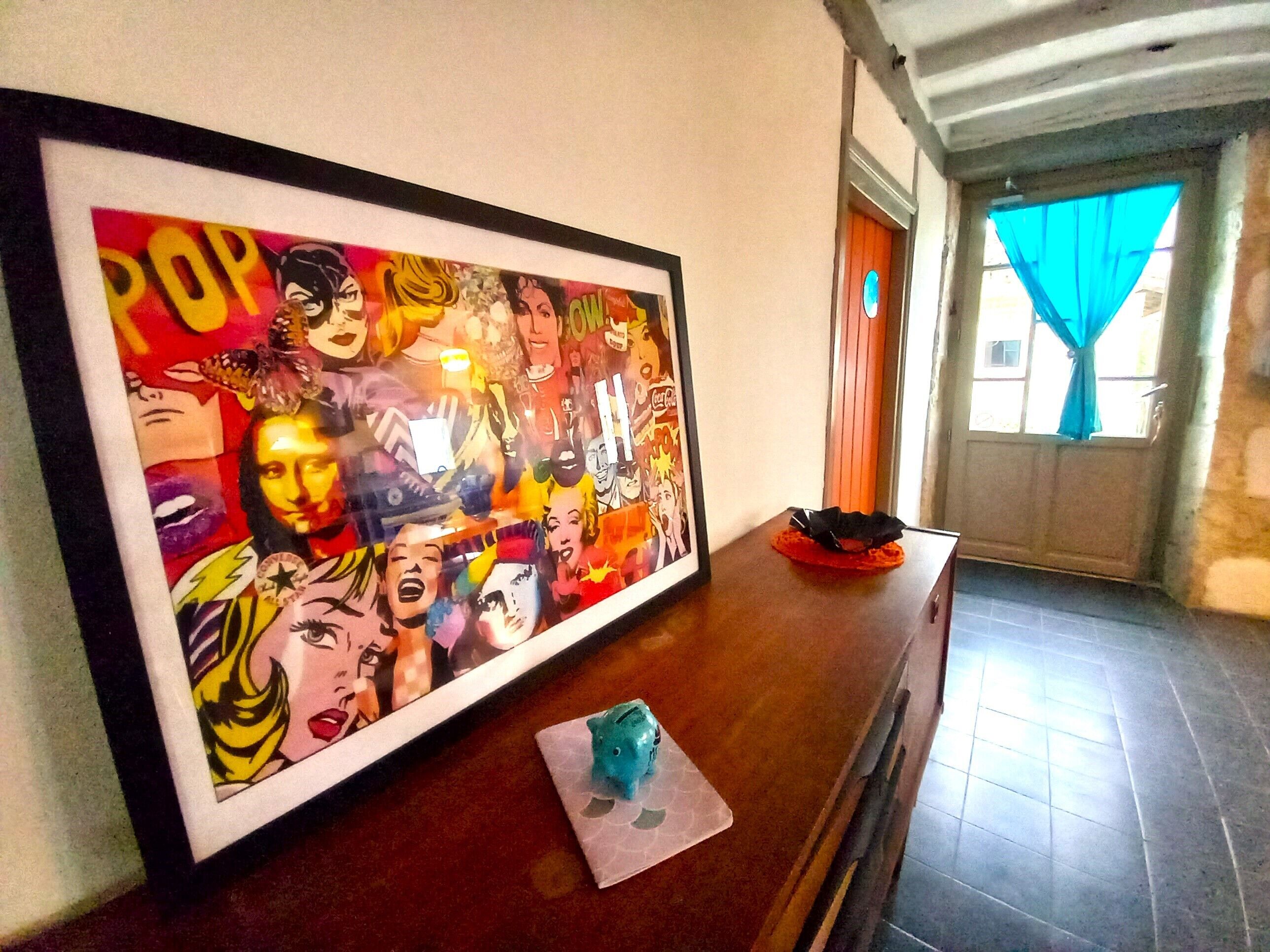 Ein gerahmtes Pop-Art-Druck an der Wand, ein kleines blaues Spielzeug auf einem Tisch und ein Fenster mit blauen Vorhängen.