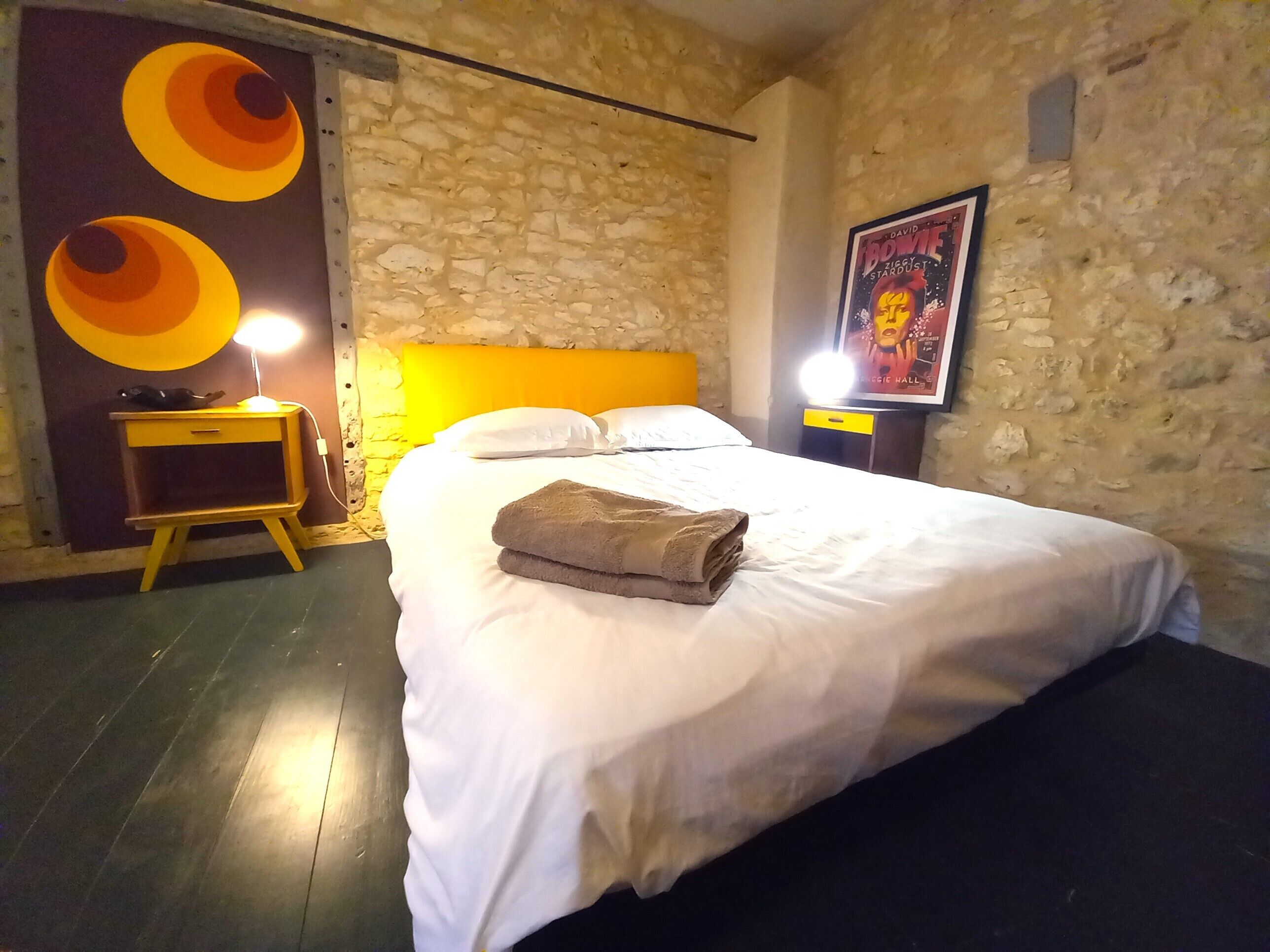 Ein Hotelzimmer mit einem großen Bett, einem Nachttisch mit Lampe, einer Steinwand und einem Poster an der Wand.