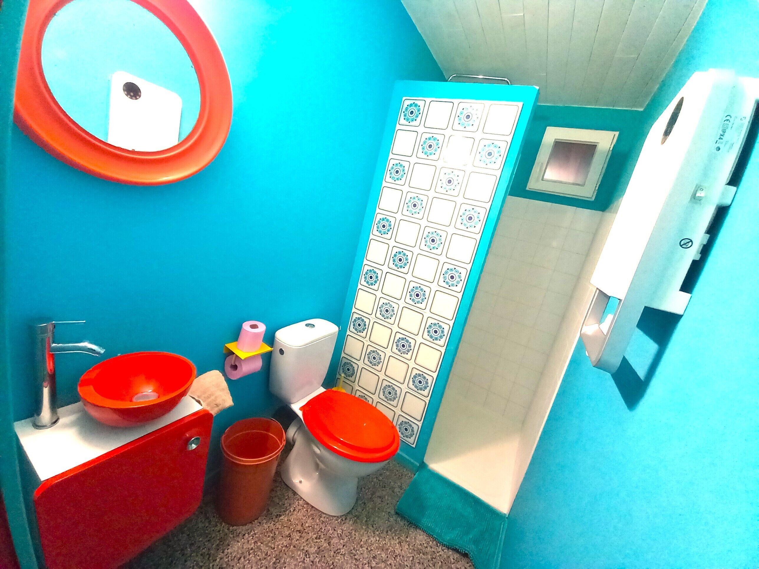 A bathroom with a blue wall, a red sink, two toilets, a mirror, and a toilet paper holder.