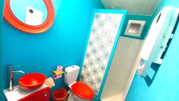 A bathroom with a blue wall, a red sink, two toilets, a mirror, and a toilet paper holder.
