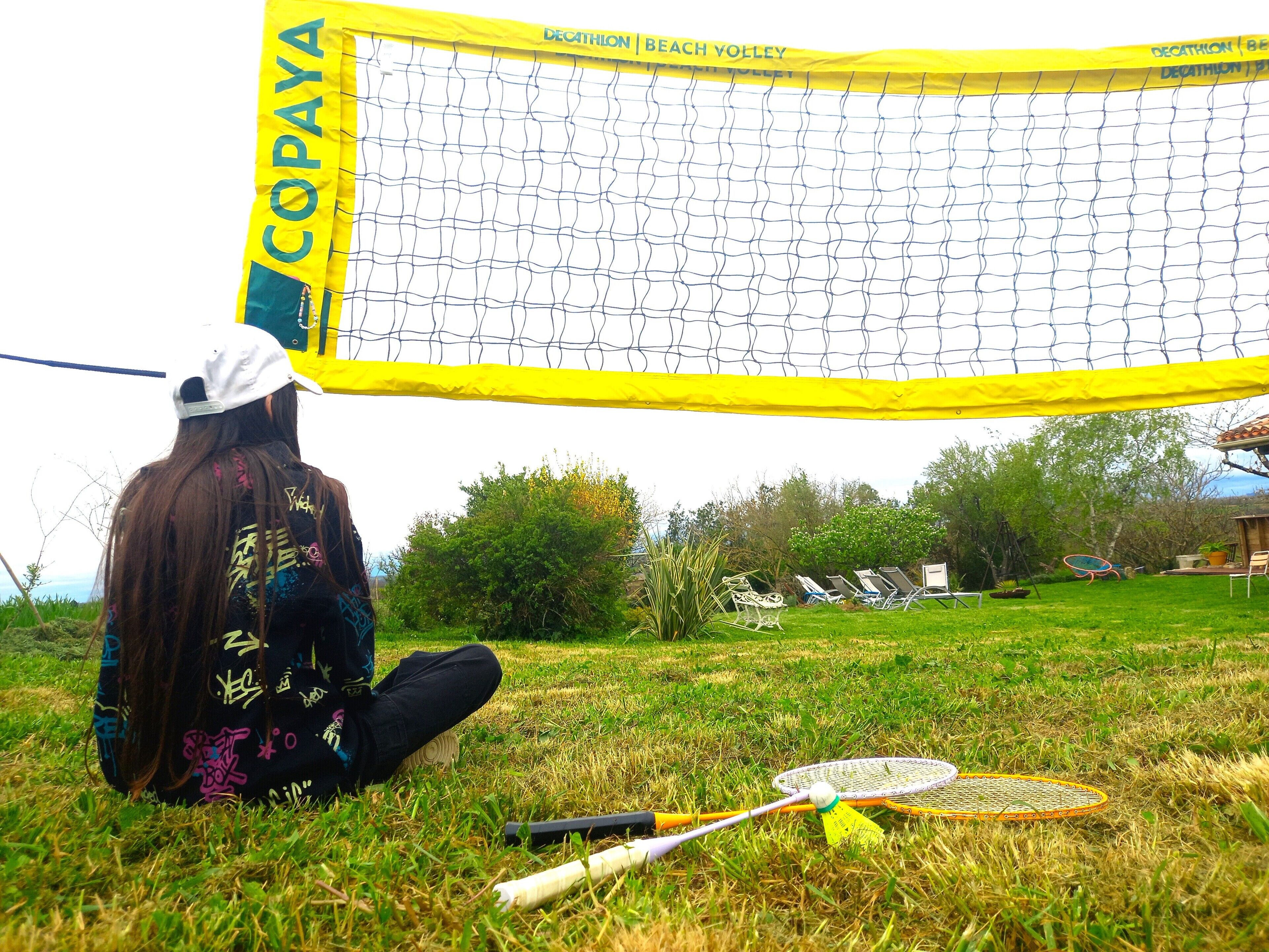 Ein Volleyballnetz mit dem Aufdruck 'COPAYA', im Vordergrund eine Person, die auf dem Gras sitzt.