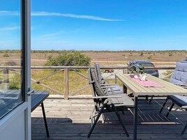 An outdoor deck with a table and chairs, a car parked nearby, and a view of the landscape.