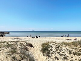 Una playa con gente, cielo despejado y agua tranquila.