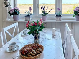 Una mesa de comedor con un centro de mesa floral, una cesta de pasteles y vistas a un campo a través del ventanal.