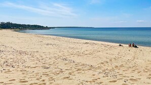 Ein Strand mit blauem Himmel, ruhigem Wasser und einigen Personen in der Ferne.