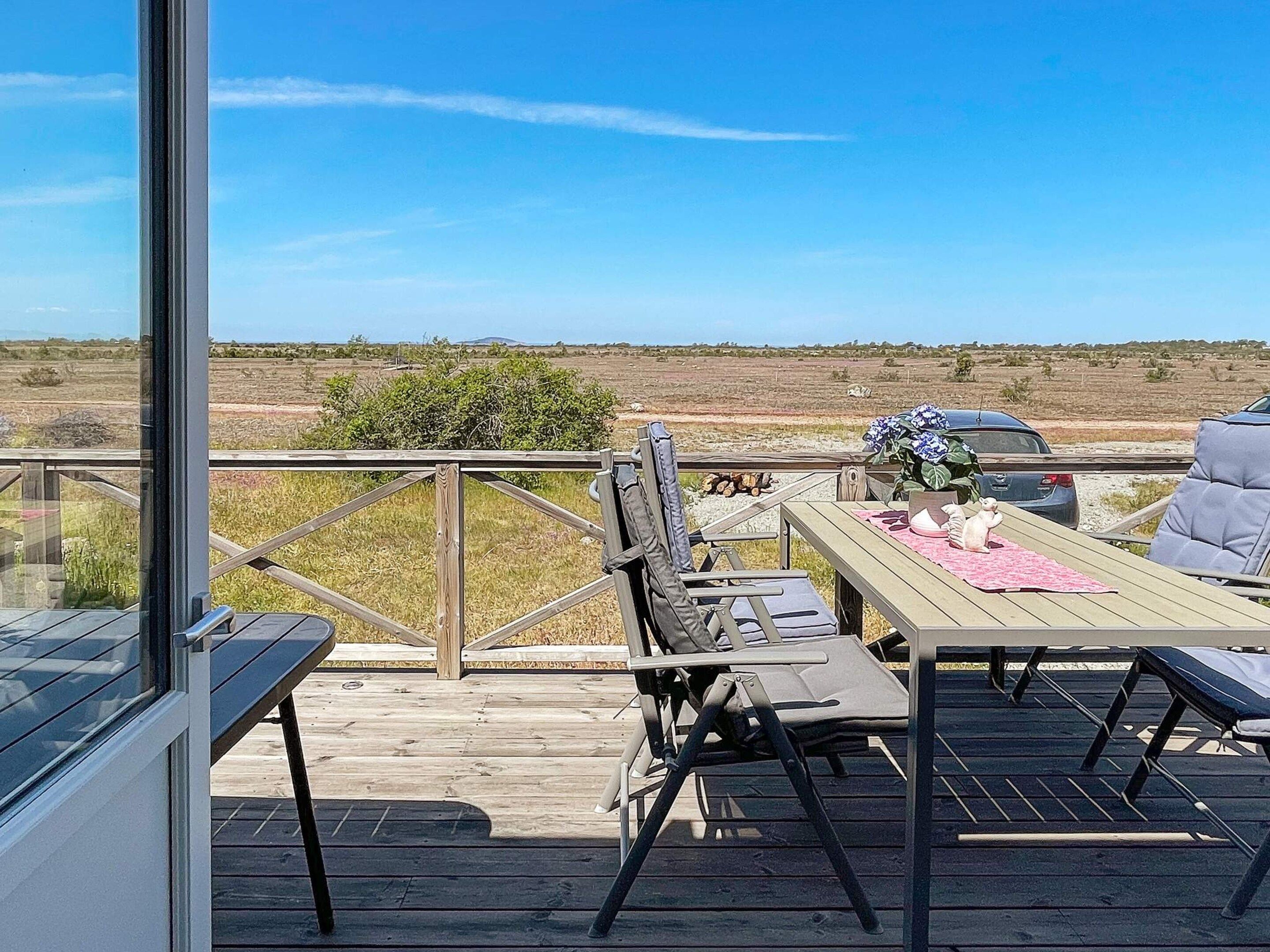 Una terraza de madera con mesa y sillas, un vidrio y vistas al paisaje.